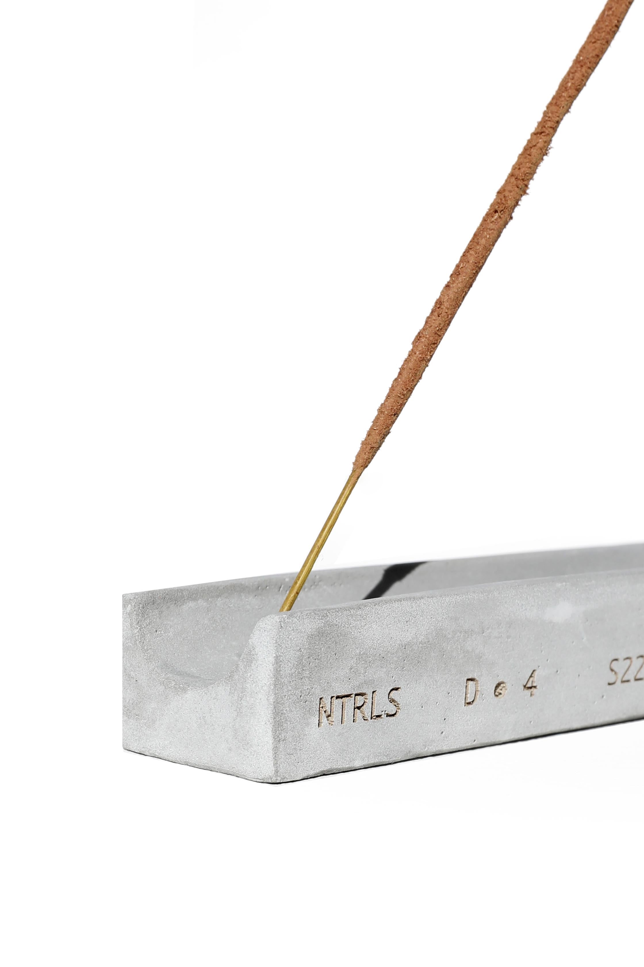 NTRLS branded concrete incense stand with burning incense. 