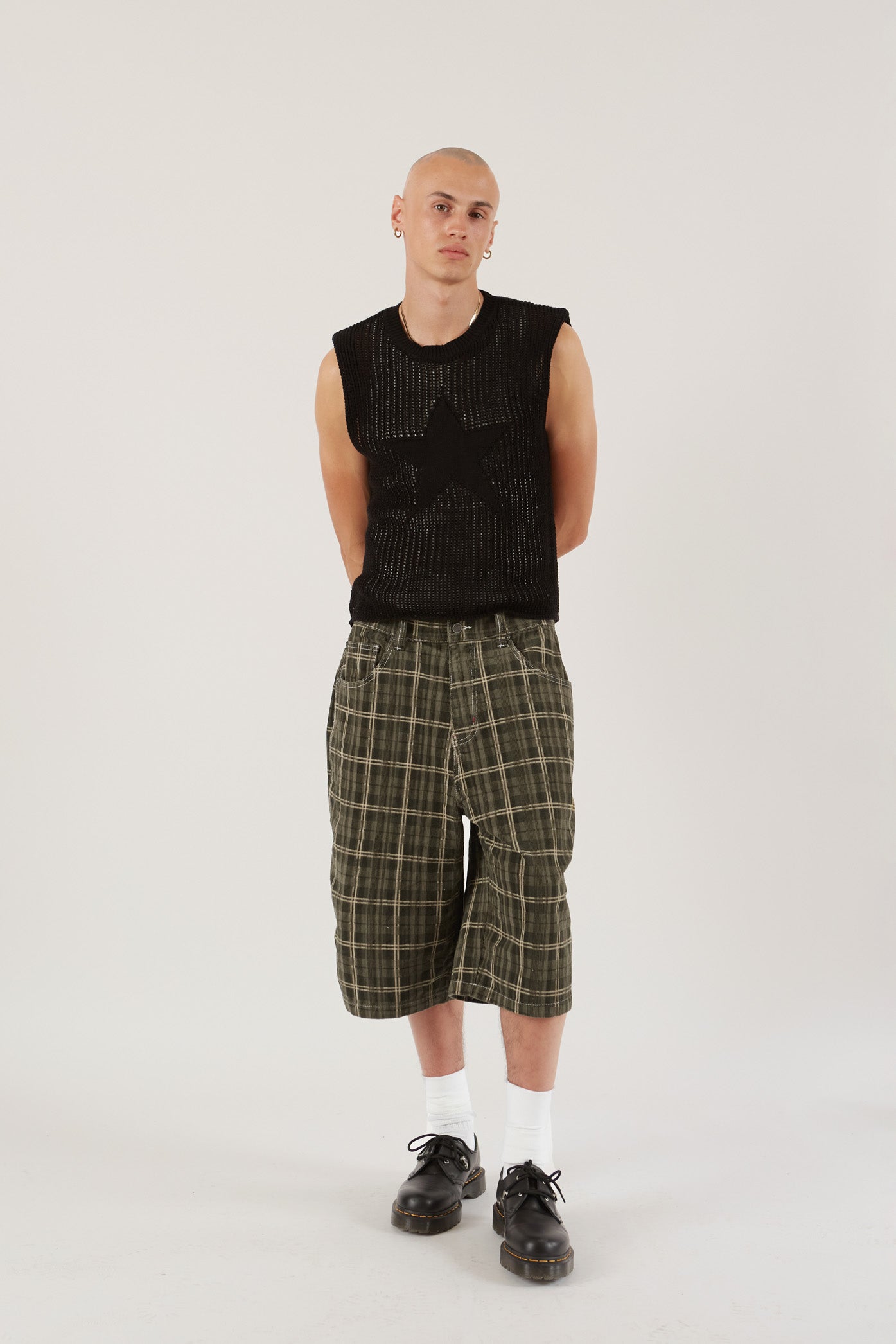 Male wearing black sleeveless knitted vest with star detail. Styled with green check oversized shorts.