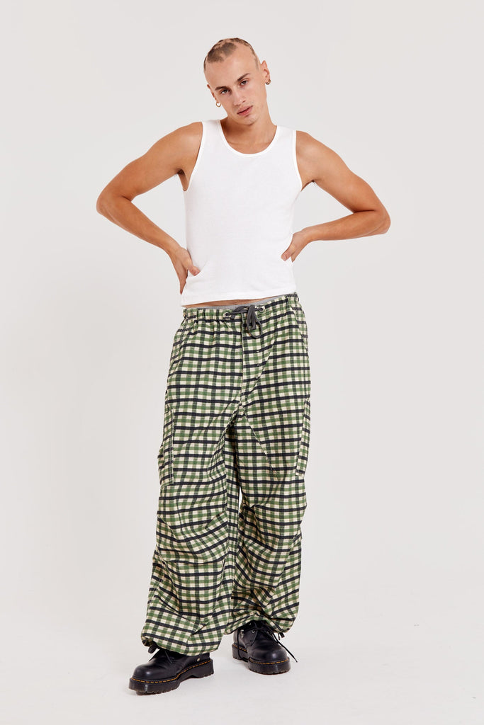 Male wearing green gingham printed check military style oversized cargo pants. Styled with a white sleeveless vest.