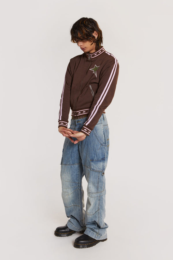 Male model wearing Light Wash Millennium Cargo Jeans styled with a brown long sleeve track top. 