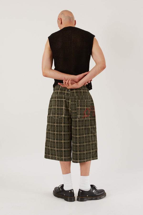 Male wearing Green Check Cord Short Jumbo Fit. Styled with black knitted sleeveless vest.