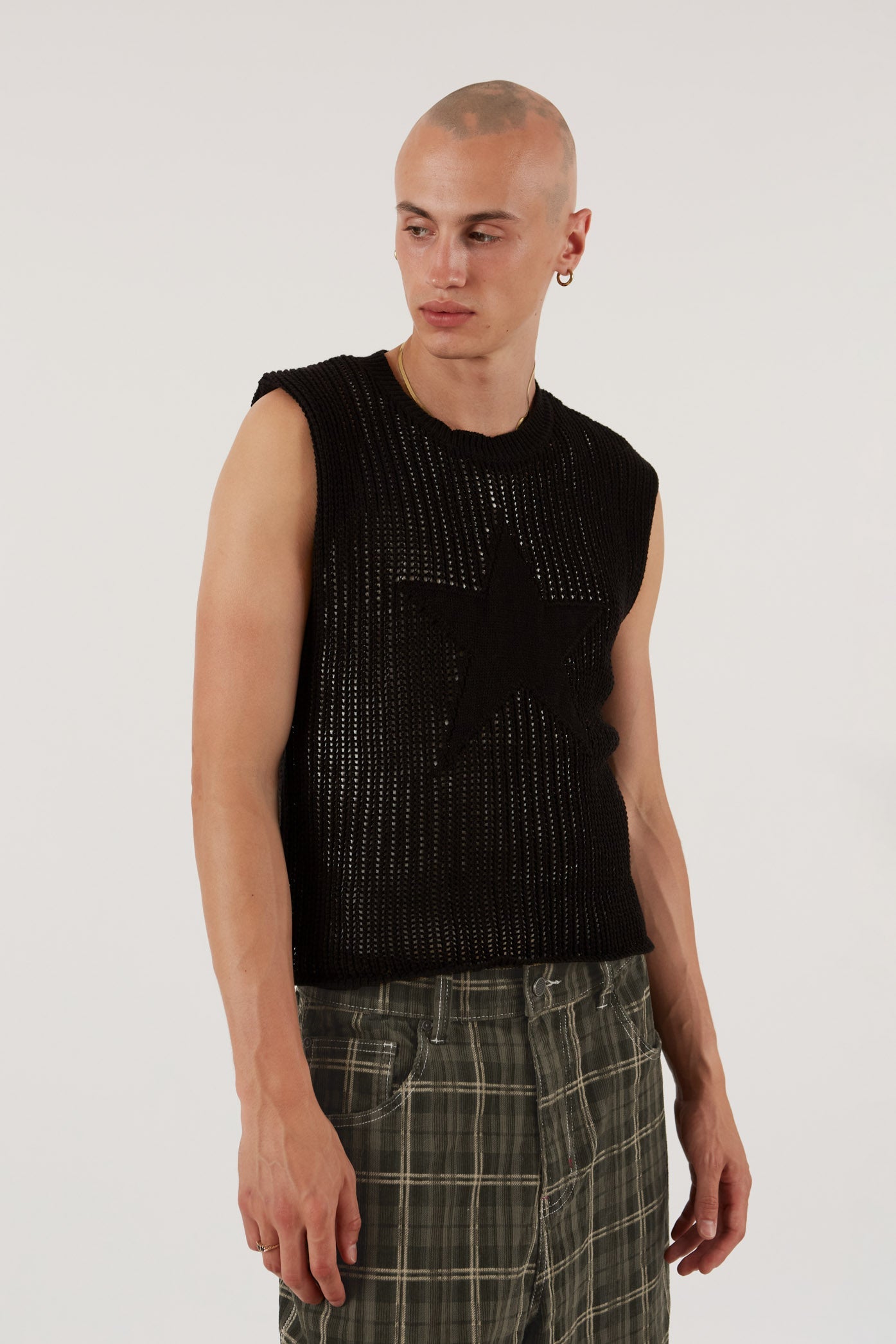 Male wearing black sleeveless knitted vest with star detail. Styled with green check oversized shorts.