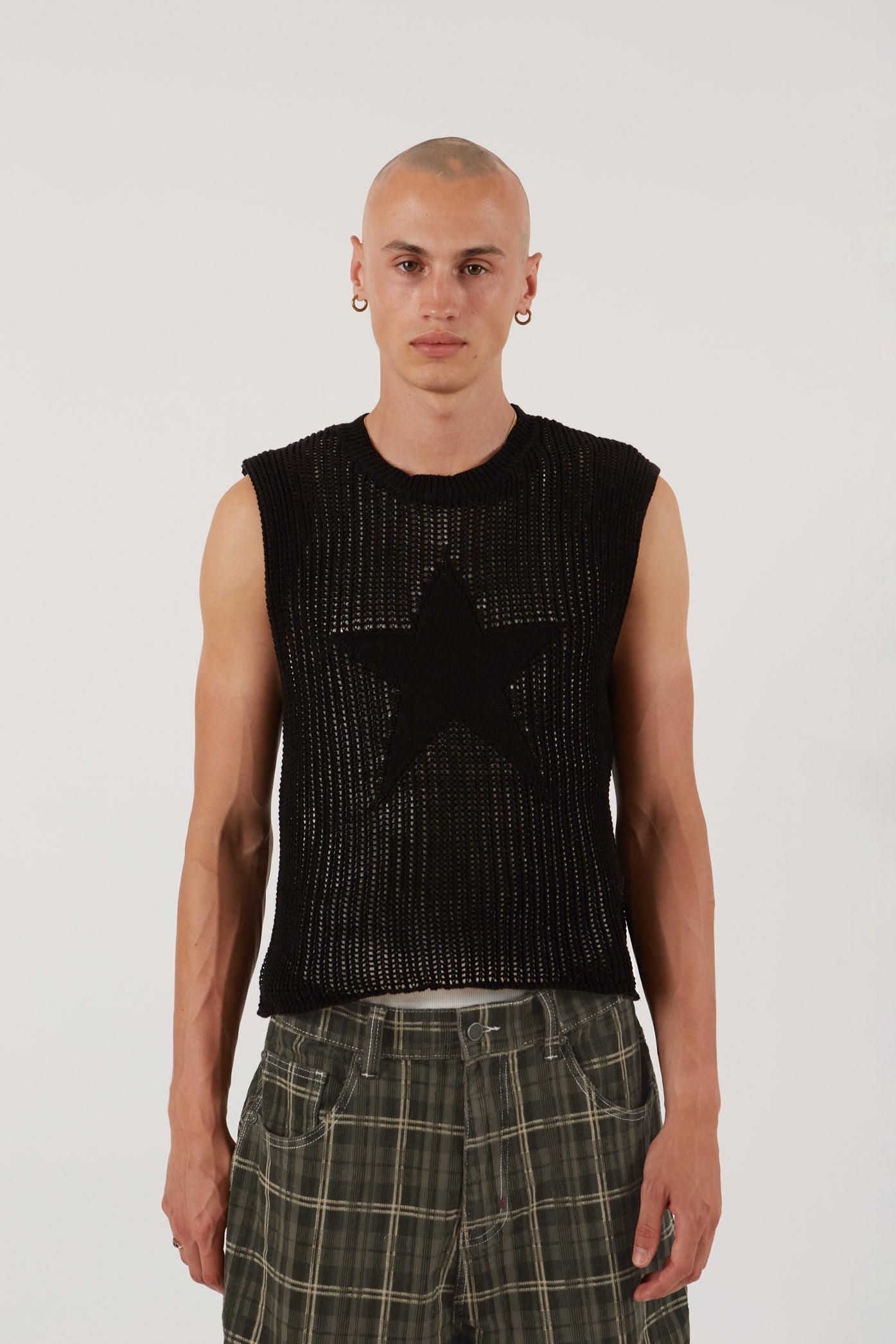 Male wearing black sleeveless knitted vest with star detail. Styled with green check oversized shorts.