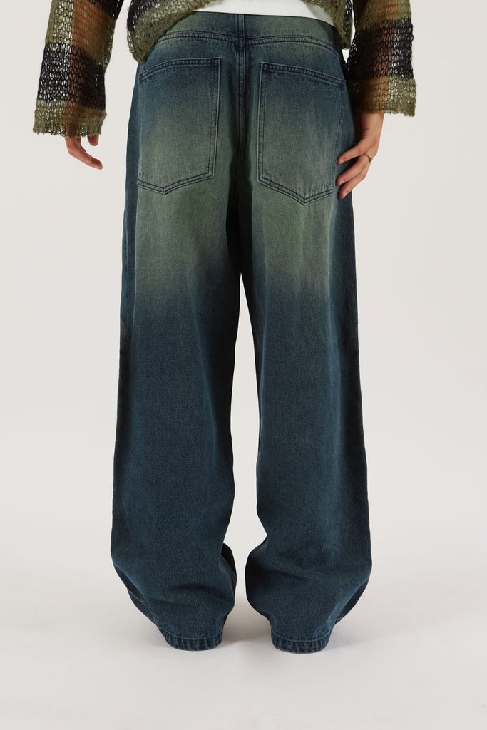 Male wearing Sandblast Oversized Skate Fit Denim Jeans. Styled with green and black knitted jumper. 