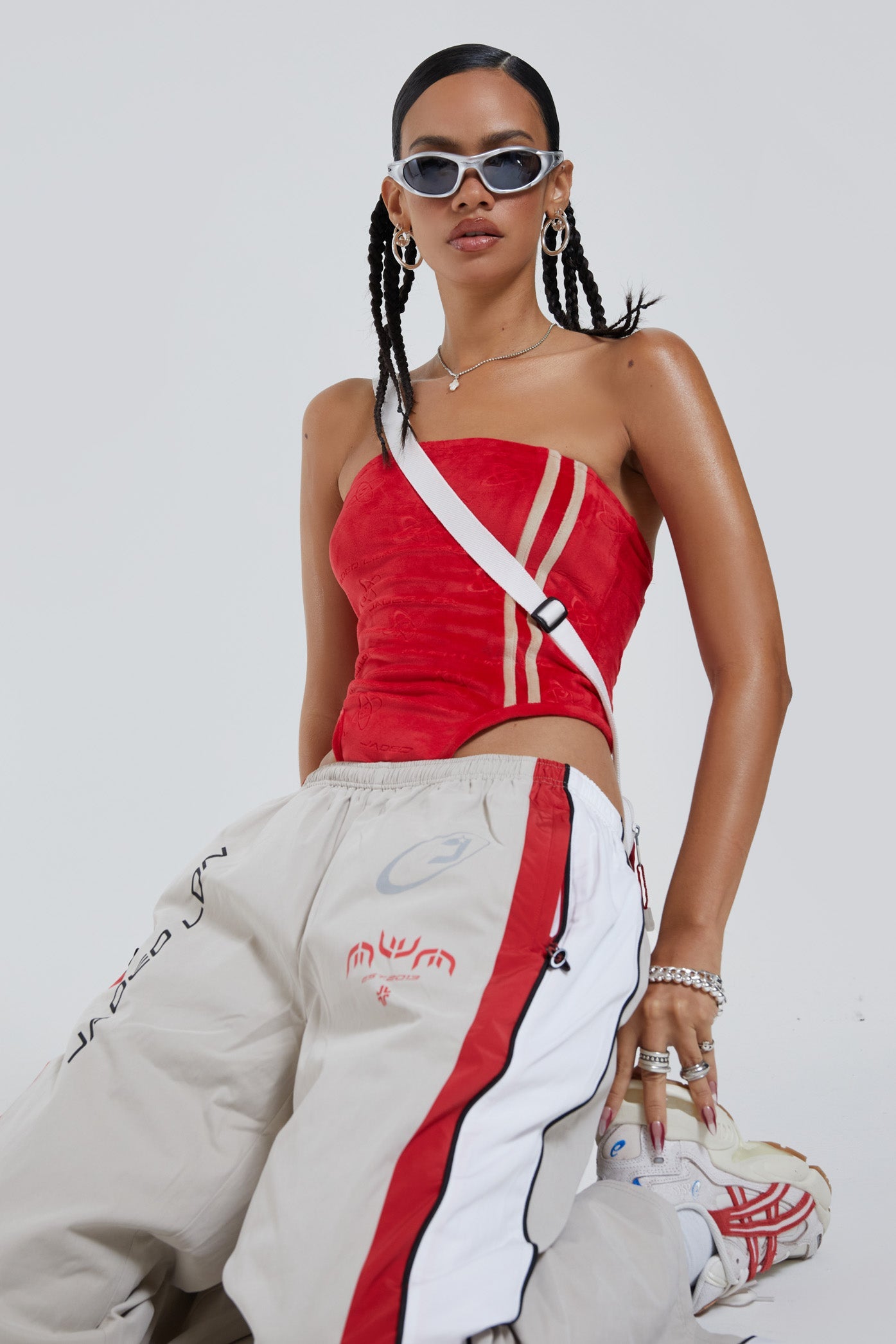 Female wearing red logo monogram embossed strapless bodysuit with stripe detail. Styled with almond track pants. 