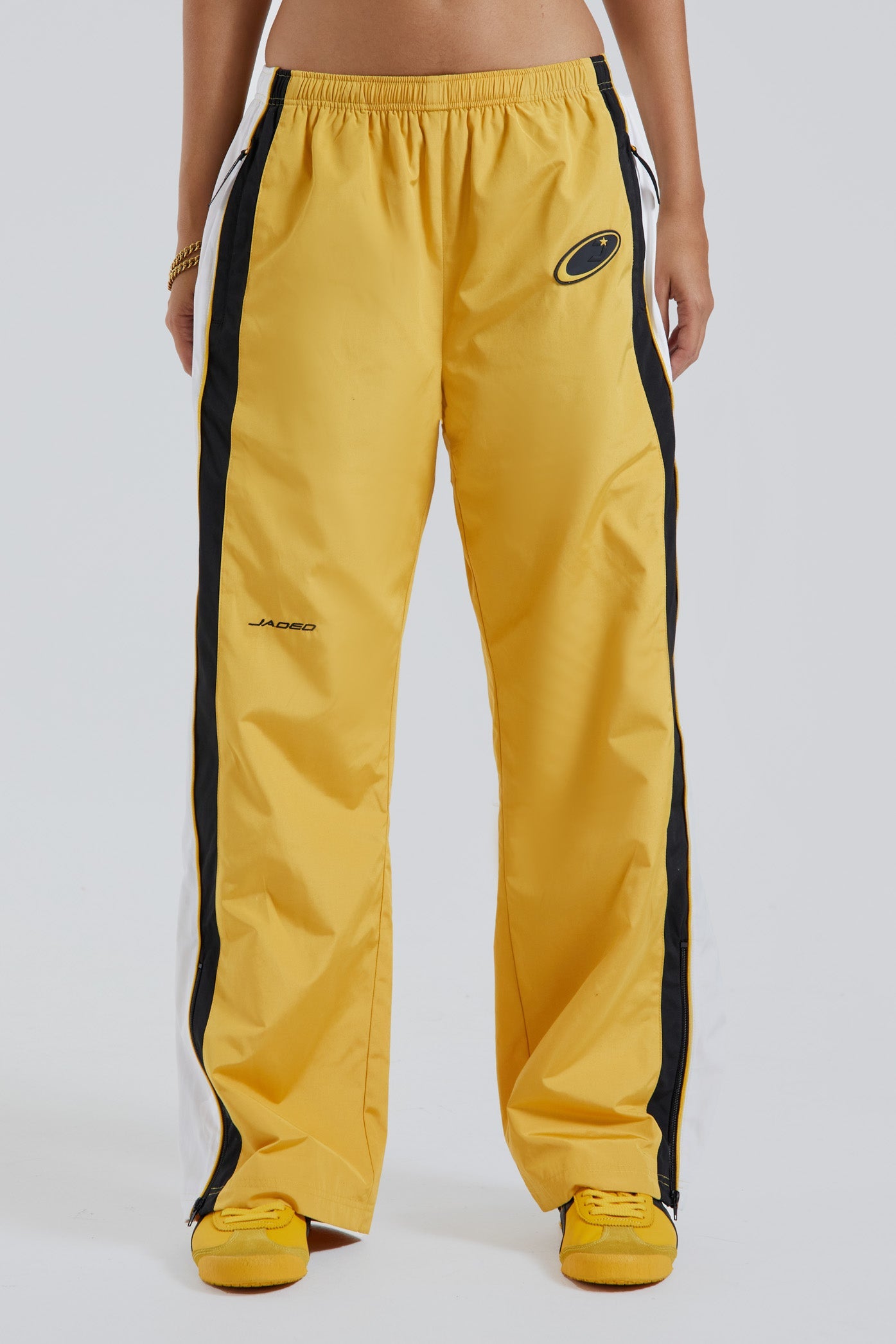 Female wearing yellow oversized drawstring waistband track pants with Jaded branding detail. 