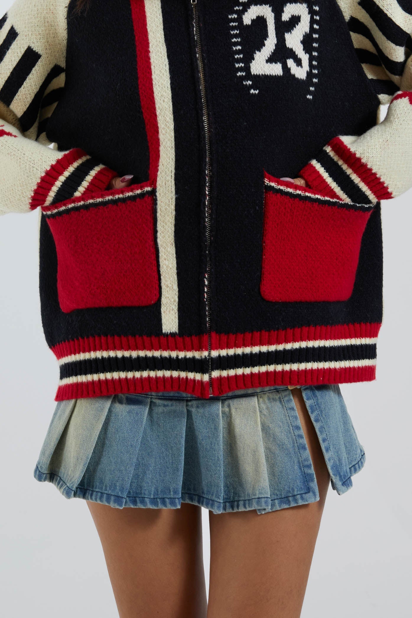 Female wearing collegiate chunky zip through long sleeve oversized jumper. Styled with blue pleated denim mini skirt. 