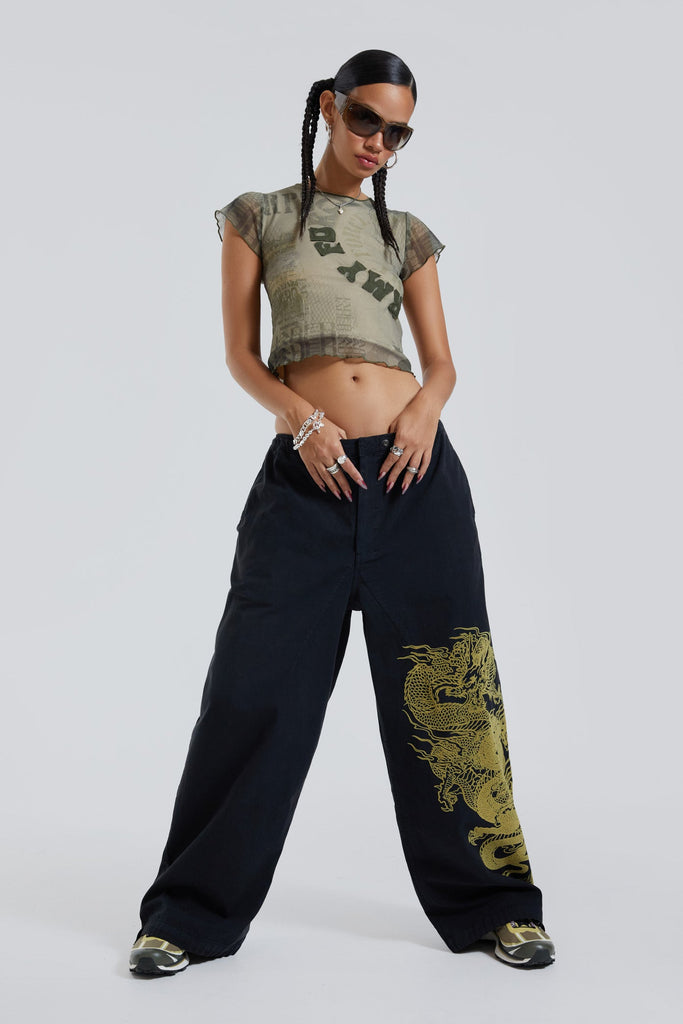 Female wearing khaki double layer mesh t-shirt with wording print and applique detail. Styled with black parachute cargo parachute pants with green dragon flock print. 