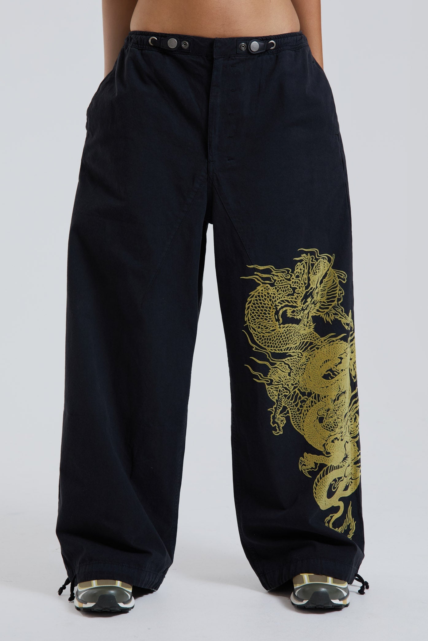 Female wearing black military cargo parachute pants with green dragon flock print. 