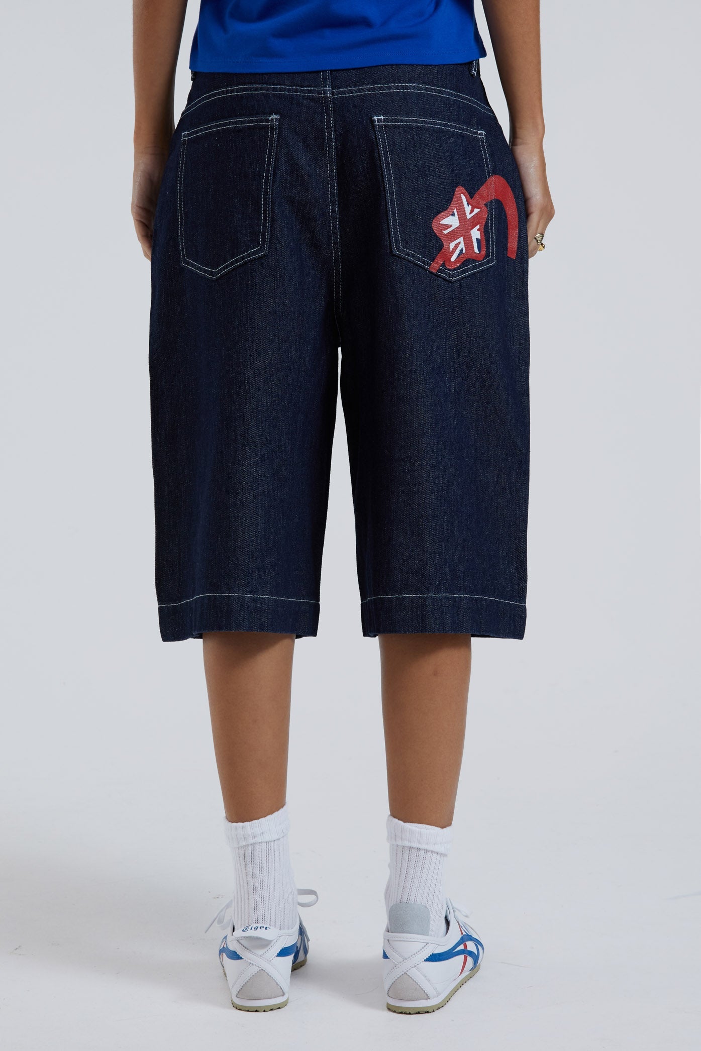 Female wearing sandblast washed denim oversized jorts in a jumbo fit with embroidered pocket patch detail. 