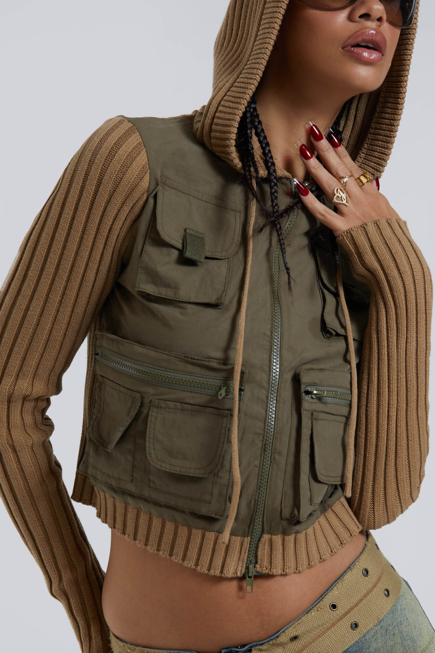 Female wearing khaki green cargo long sleeve track jacket with ribbed knit sleeve and hood detail. Styled with blue denim jeans. 