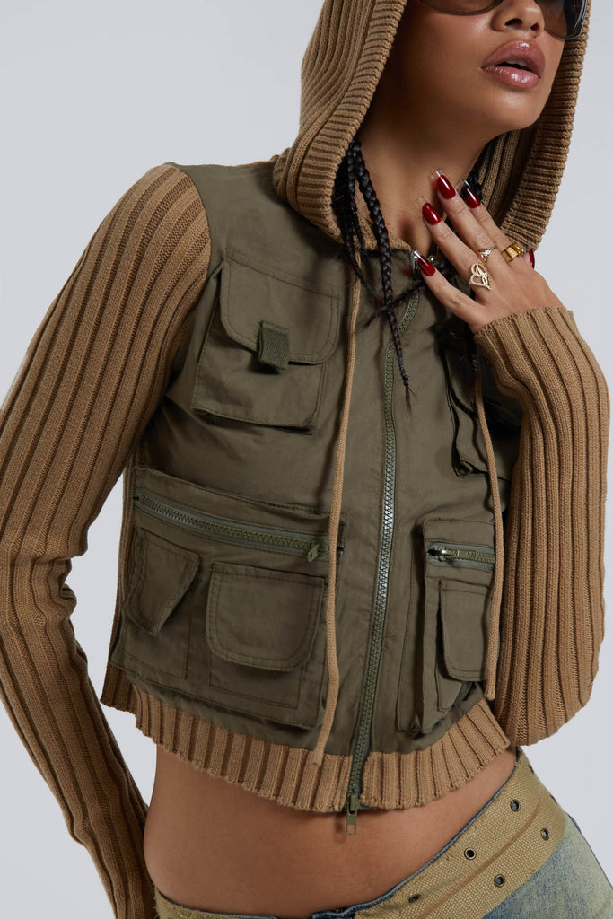 Female wearing khaki green cargo long sleeve track jacket with ribbed knit sleeve and hood detail. Styled with blue denim jeans. 