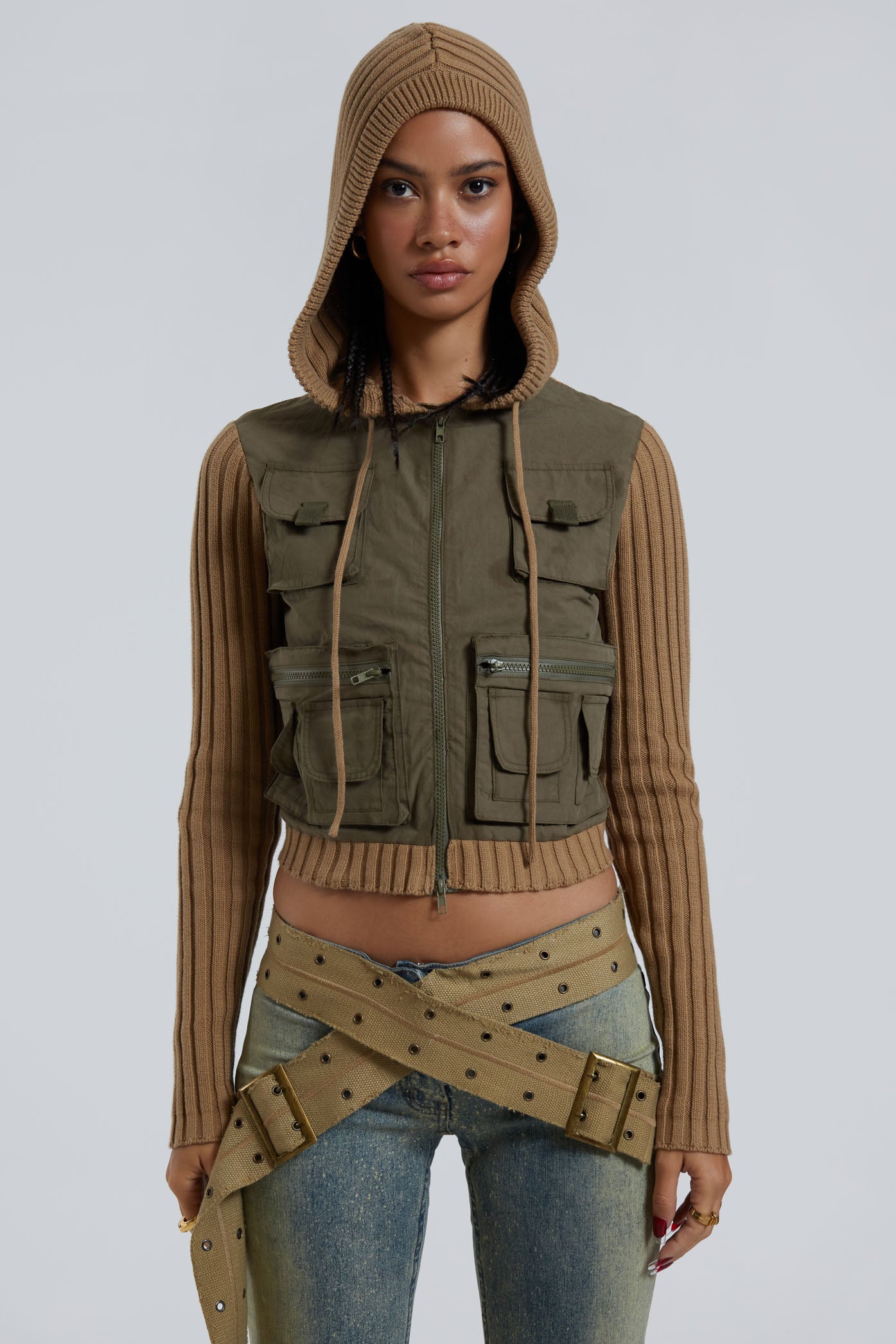 Female wearing khaki green cargo long sleeve track jacket with ribbed knit sleeve and hood detail. Styled with blue denim jeans. 