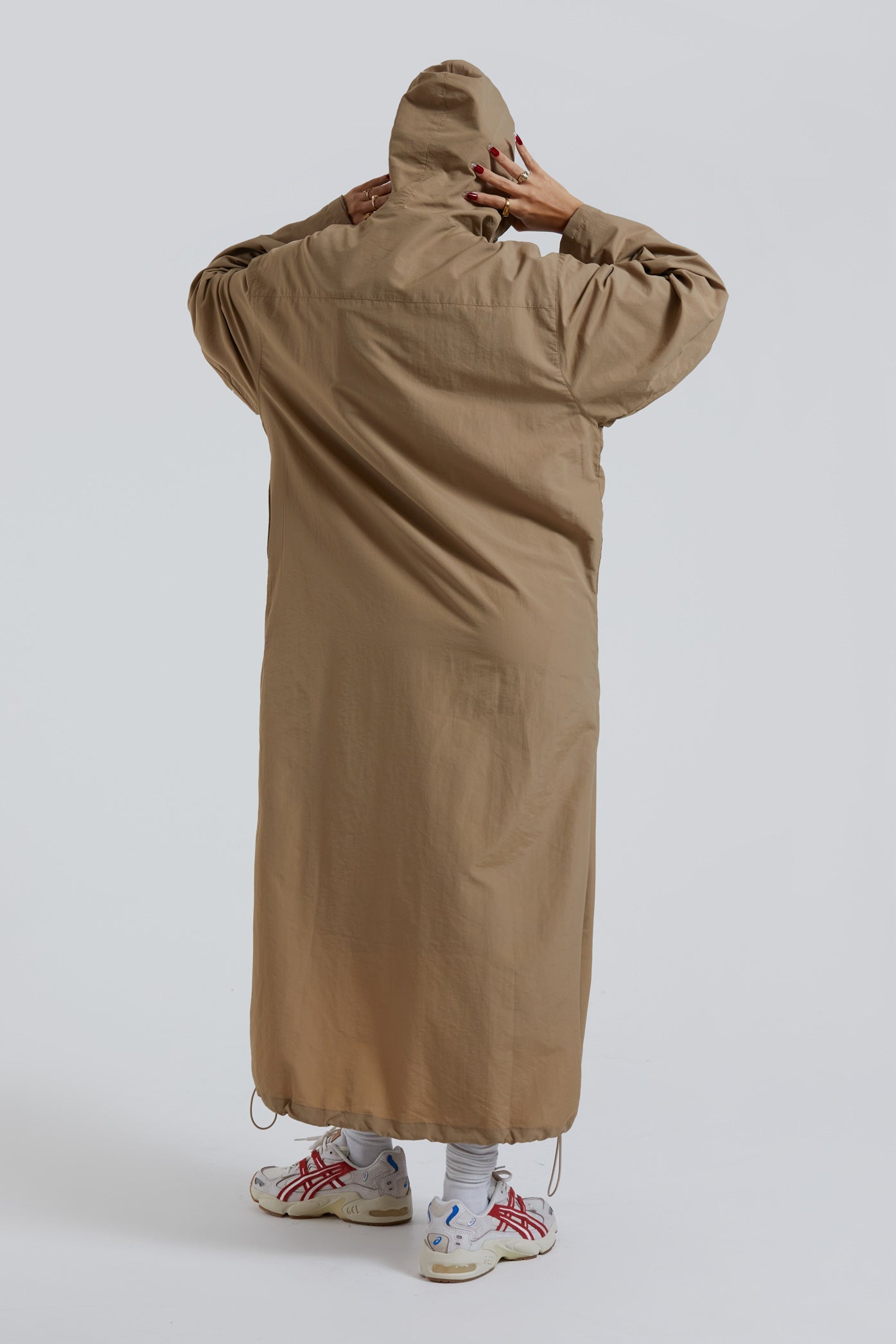 Female wearing stone khaki adjustable ruched detail maxi length long sleeve nylon jacket. 