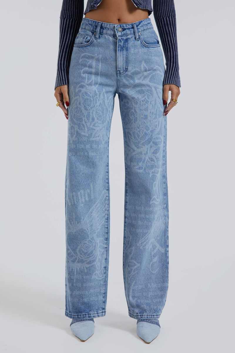 Female wearing Jaded Graffiti Discharge Print Slouchy Fit Boyfriend Jeans. Styled with blue ribbed knitted top.