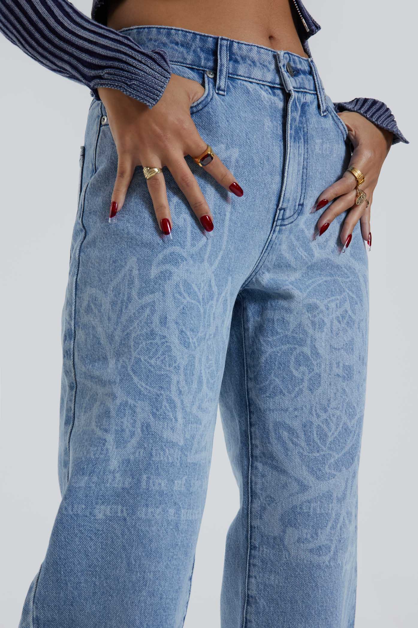 Female wearing Jaded Graffiti Discharge Print Slouchy Fit Boyfriend Jeans. Styled with blue ribbed knitted top.