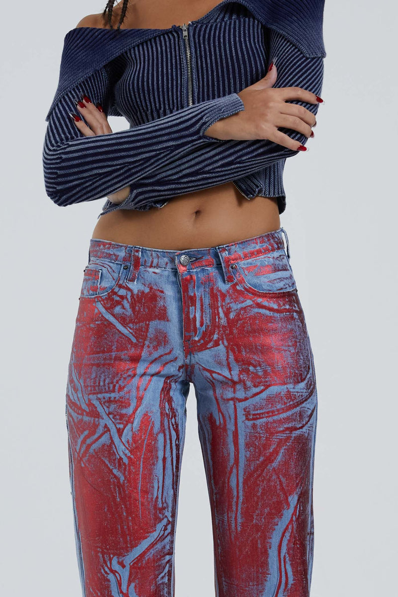 Female wearing blue and red distressed foil low rise fit 00’s style jeans. Styled with long sleeve blue knitted cardigan. 