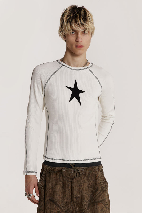 Male model wearing an off white shrunken fit long sleeve top curated in a heavy rib fabric with an applique raw edge star detail.