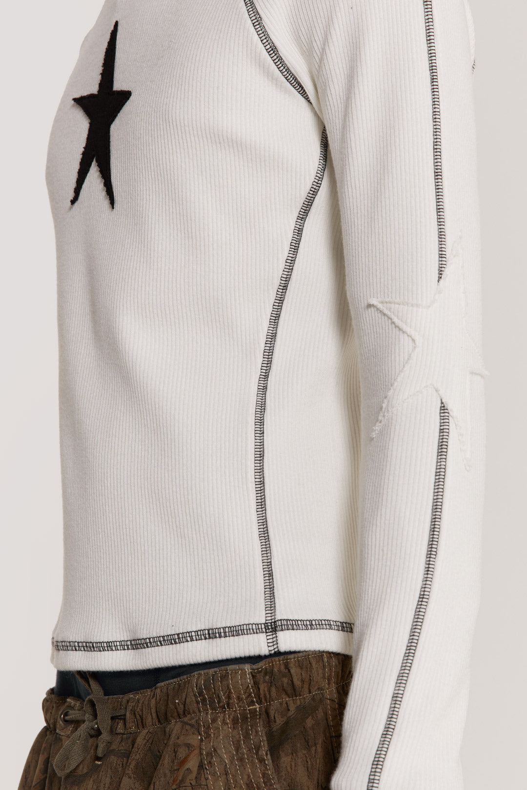 Male model wearing an off white shrunken fit long sleeve top curated in a heavy rib fabric with an applique raw edge star detail.