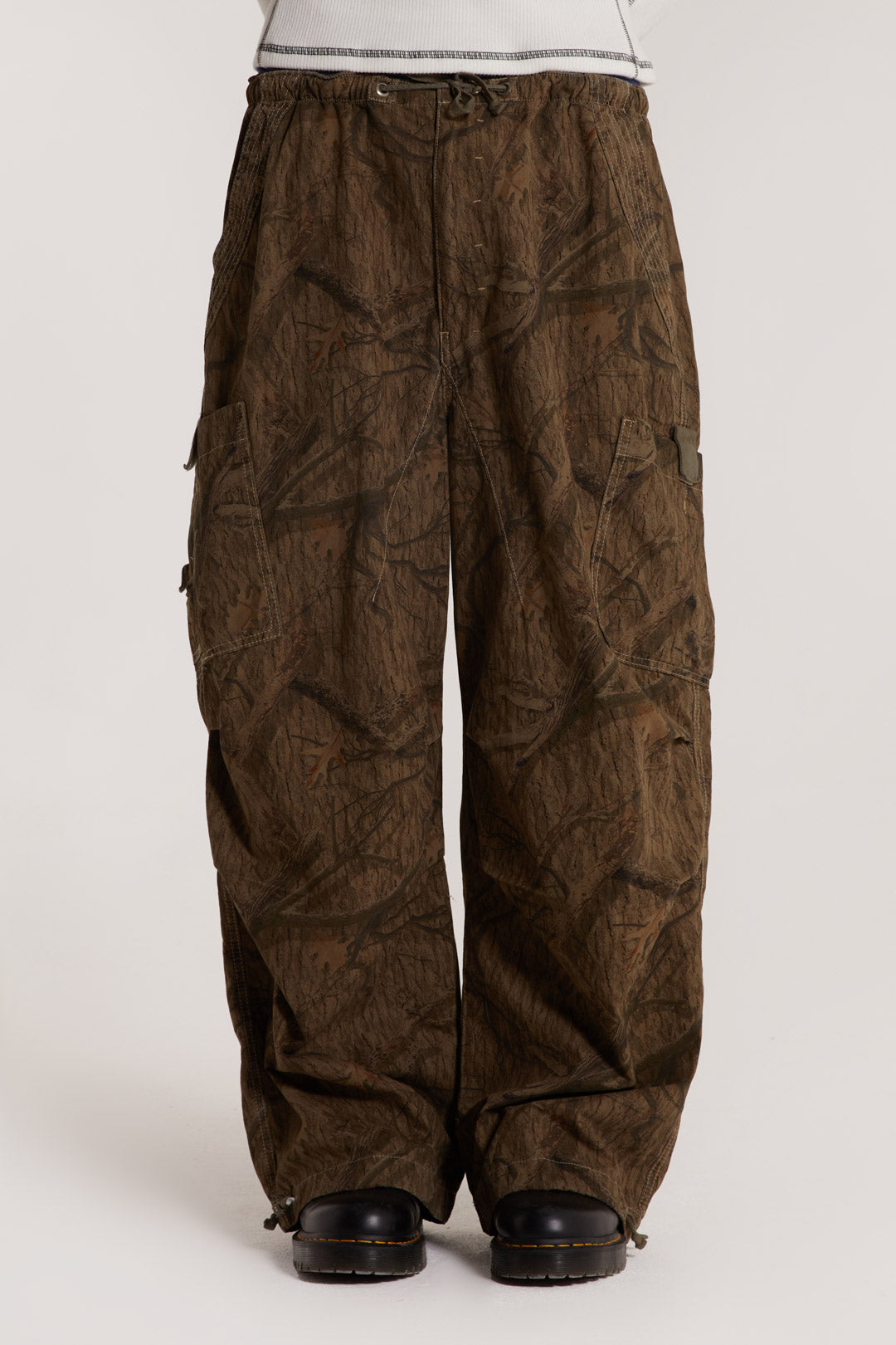 Male model wearing camouflage print parachute pants explore our take on the utility trend. The pants are fully adjustable in an oversized fit.