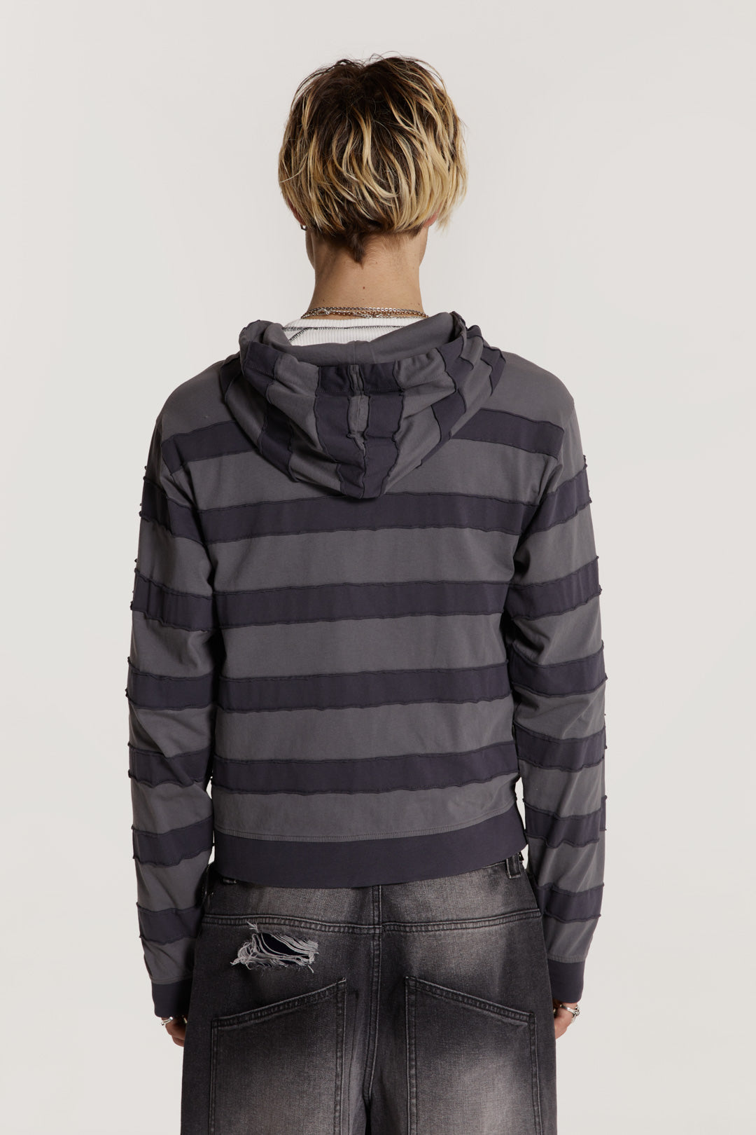 Male model wearing a grey tonal applique stripe jersey hoodie features a kangaroo patch pocket in a shrunken fit. 