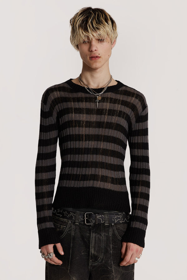 Male model wearing a black and grey striped jumper in a shrunken fit. 
