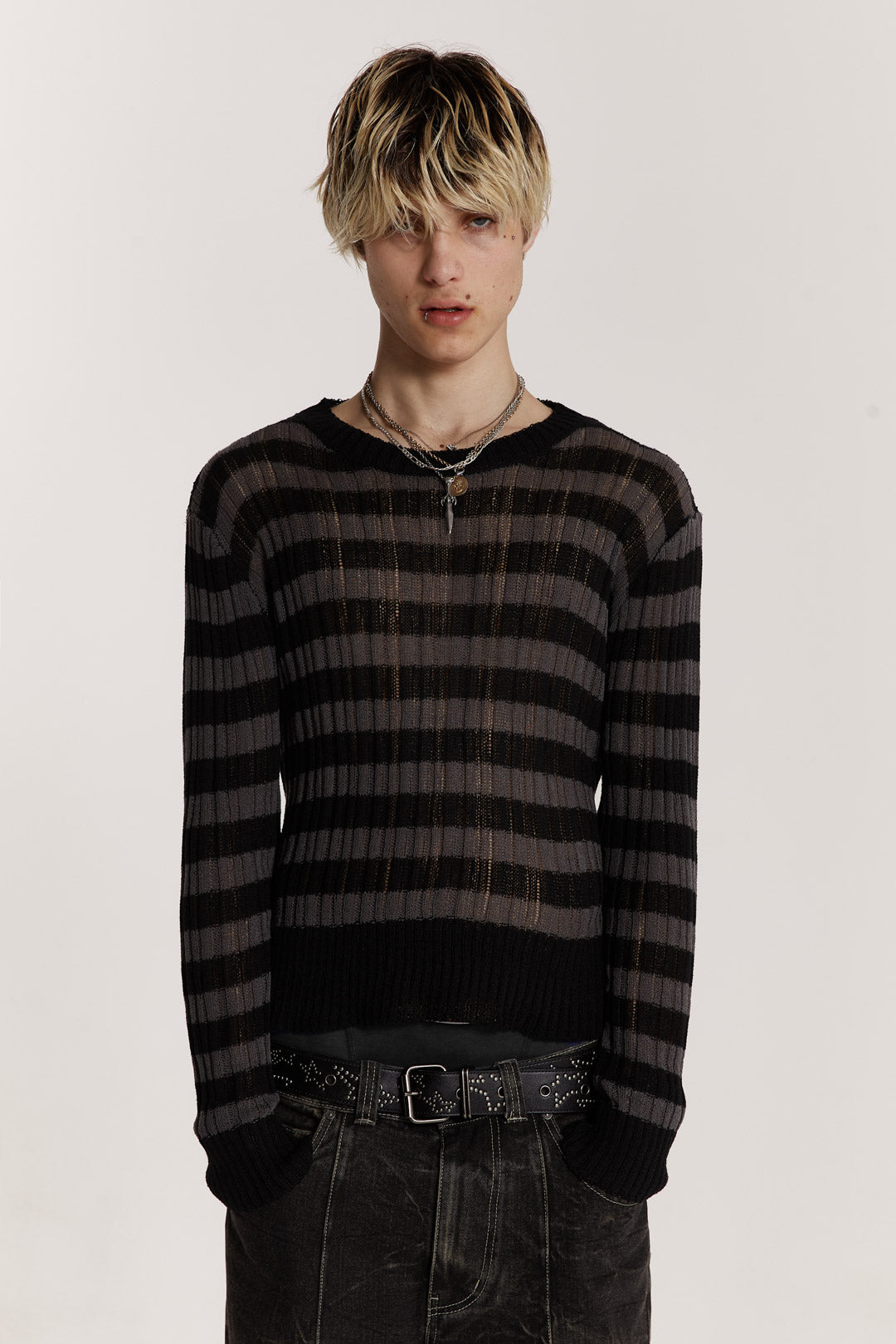 Male model wearing a black and grey striped jumper in a shrunken fit. 