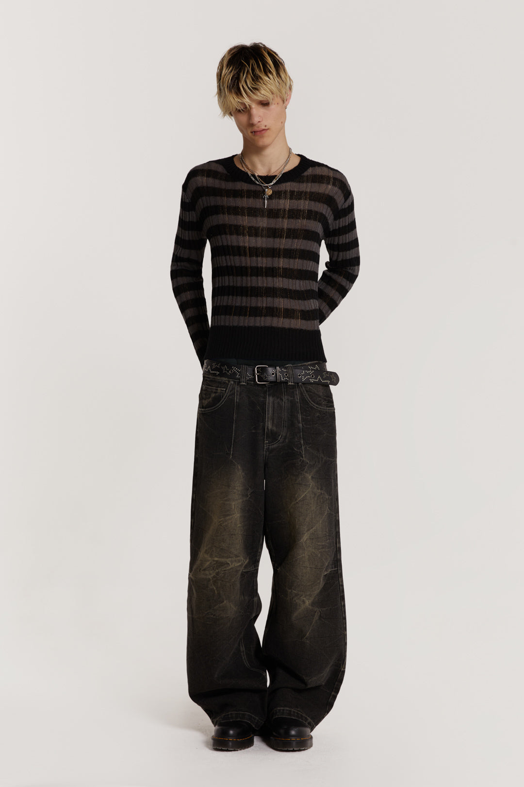 Male model wearing a black and grey striped jumper in a shrunken fit. 