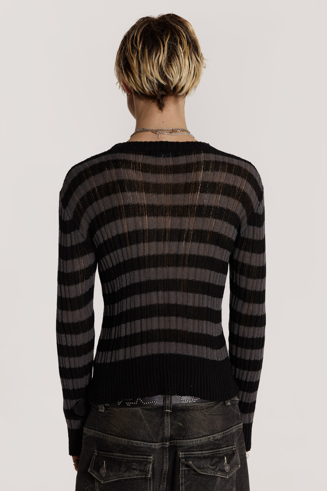 Male model wearing a black and grey striped jumper in a shrunken fit. 