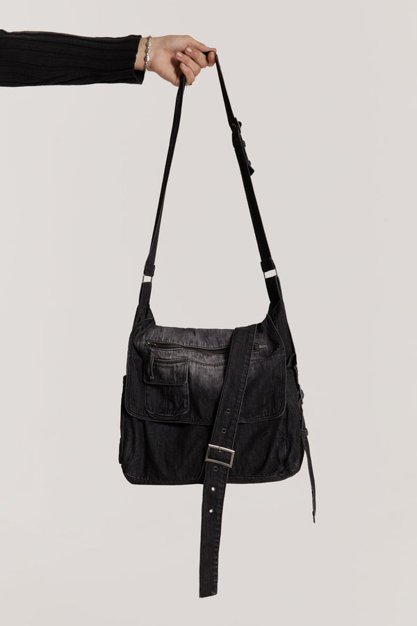 This washed black messenger bag is crafted in a washed black broken twill denim which features cargo pockets and an adjustable wrap around strap.