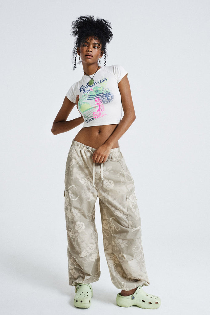 Female wearing Hawaii Vintage Graphic Baby Tee. Styled with floral tonal parachute pants. 