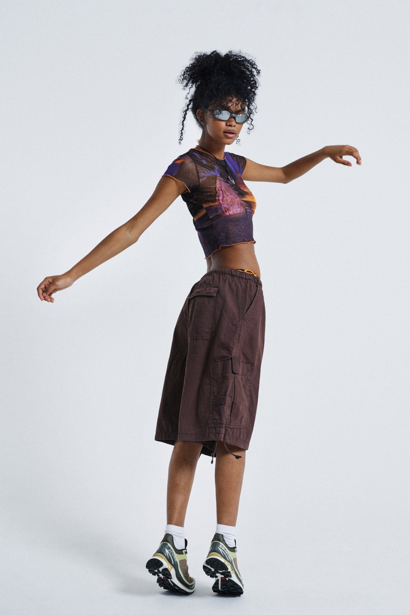 Female wearing Sunset Print Vintage Mesh Baby Tee. Styled with brown oversized parachute shorts.