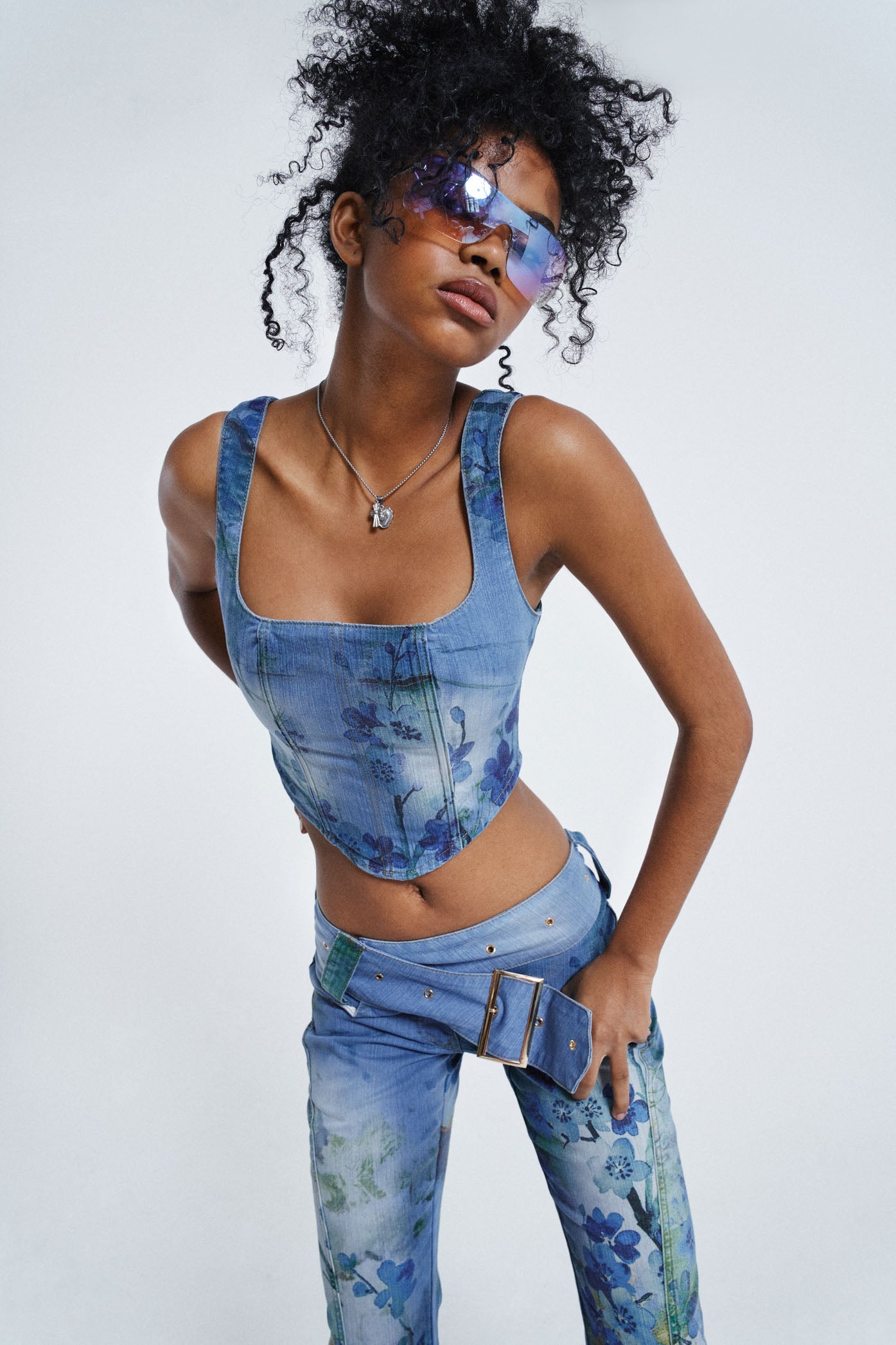 Female wearing Blue Floral Denim Corset Top. Styled with the matching floral jeans.