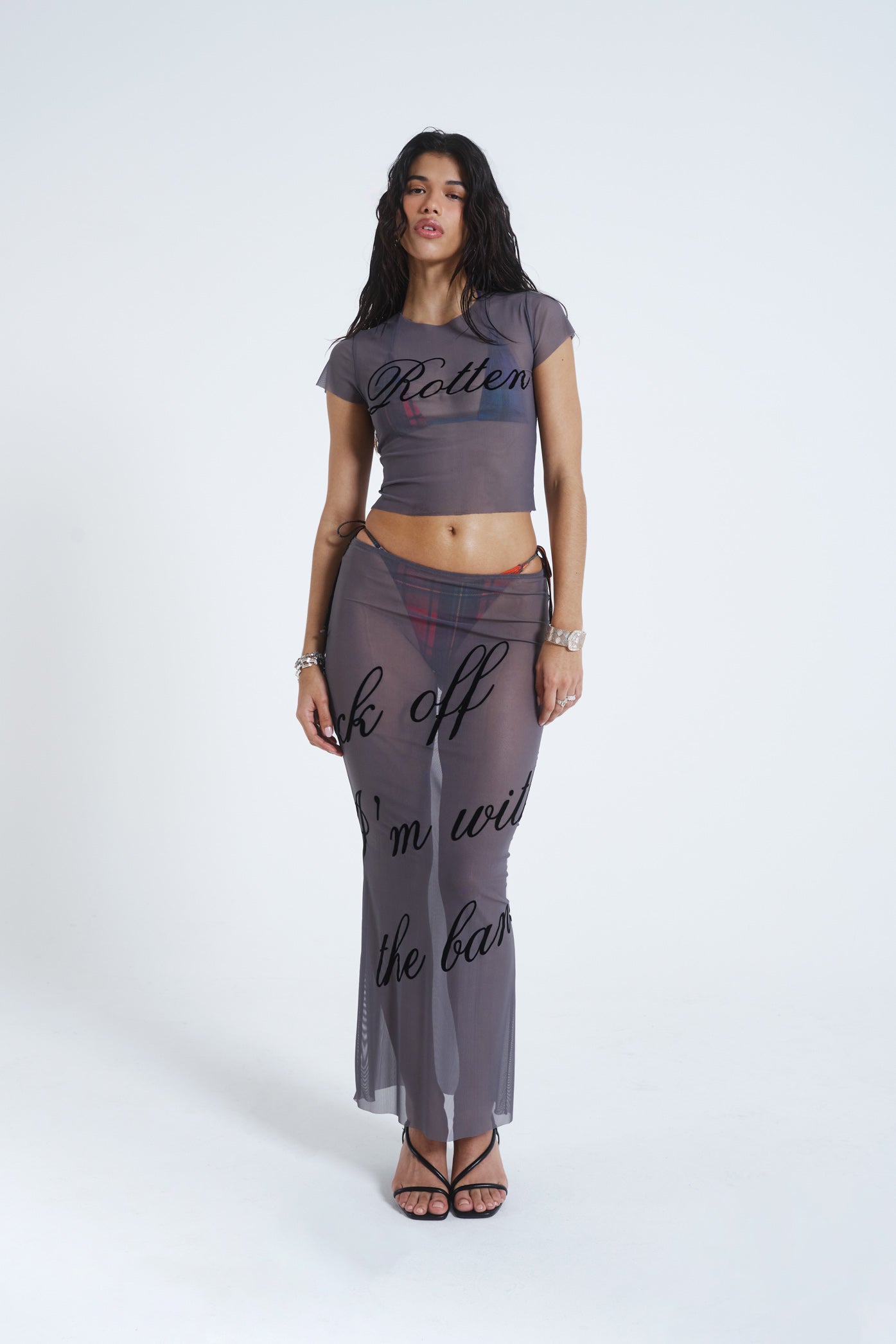 Female model wearing grey lightweight mesh t-shirt features a “rotten” black flock placement print. Paired with the matching mesh maxi skirt. 