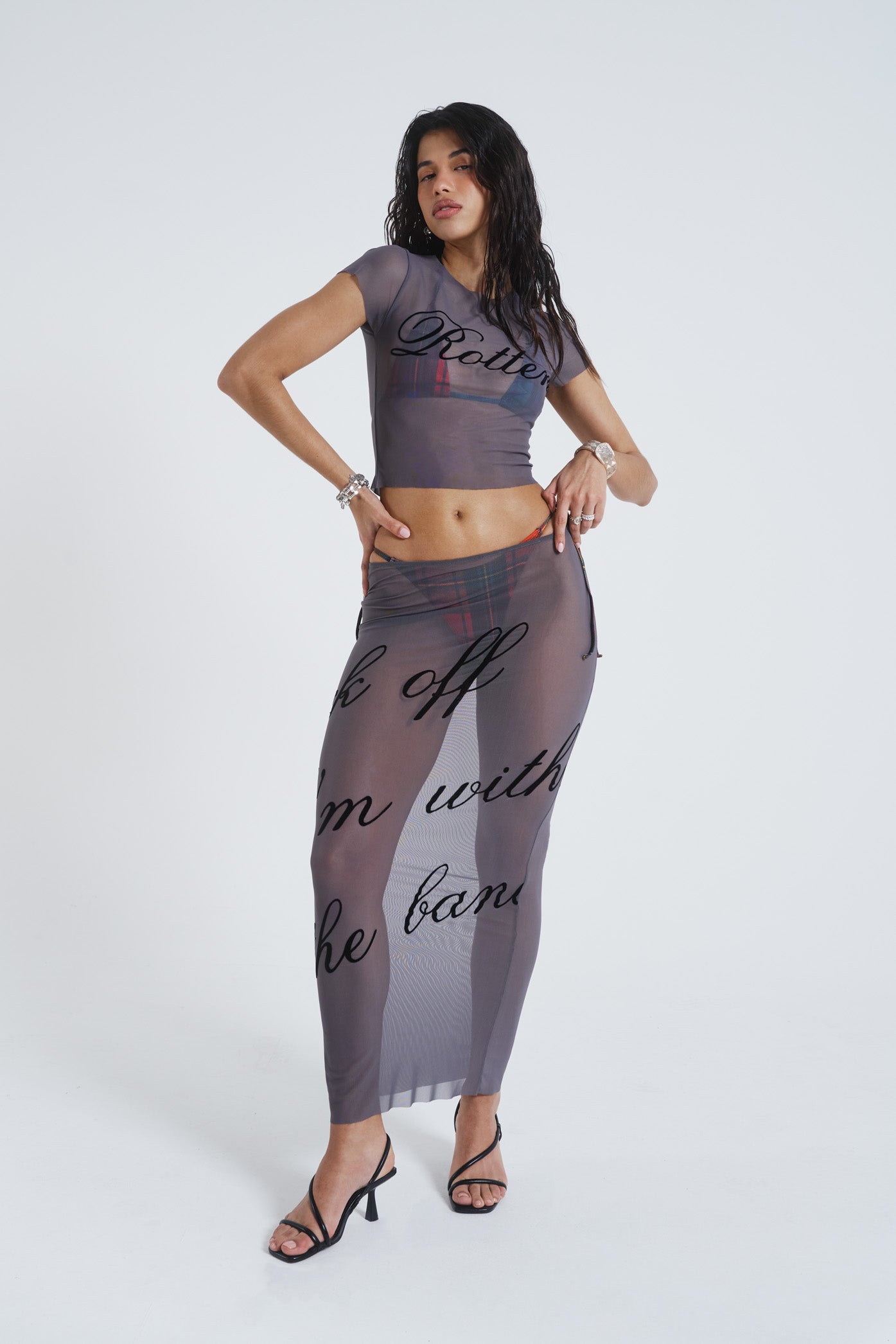 Female model wearing grey lightweight mesh t-shirt features a “rotten” black flock placement print. Paired with the matching mesh maxi skirt. 