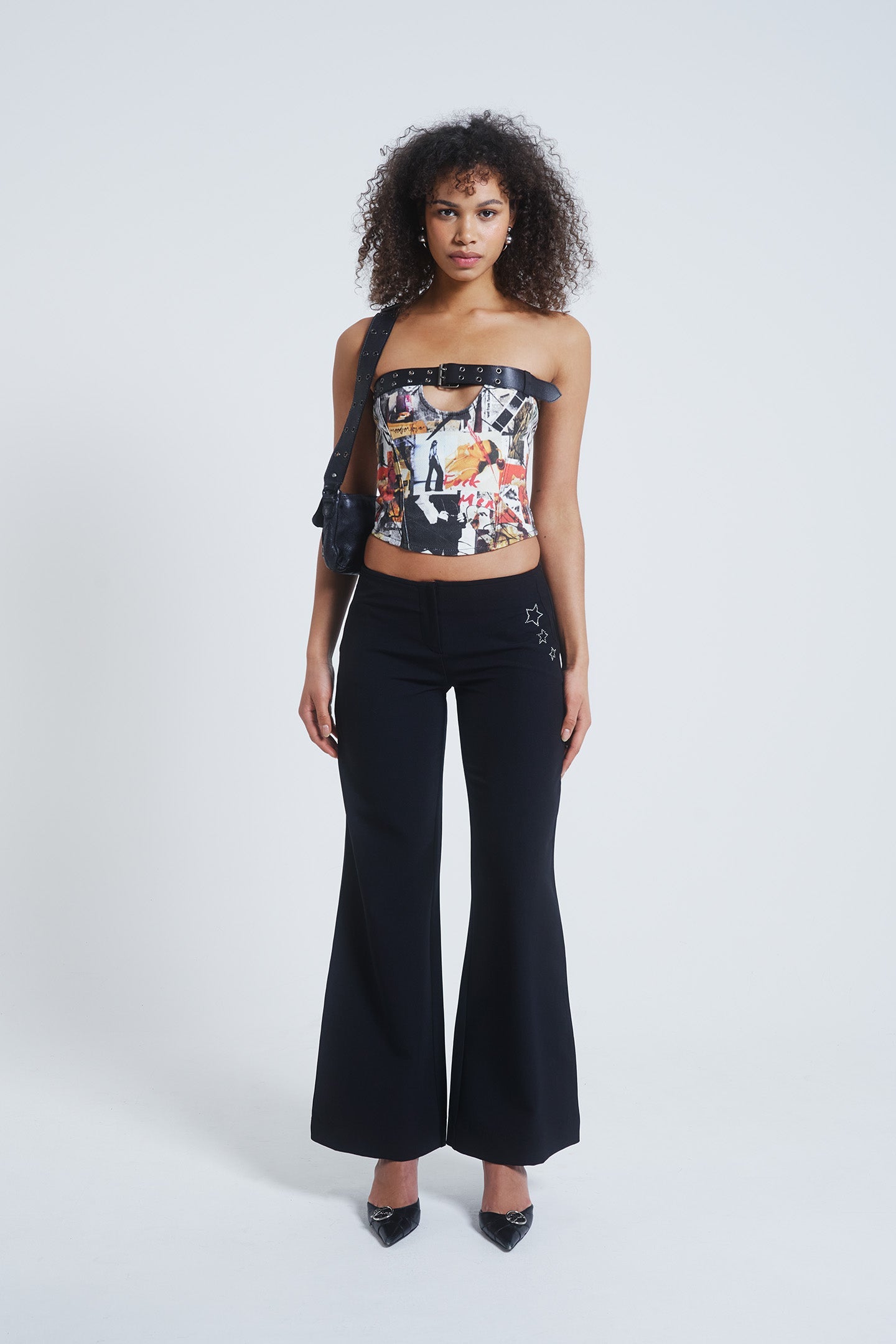 Female model wearing a mixed magazine print corset top with cut out and black belt detail. Paired with black flared trousers.