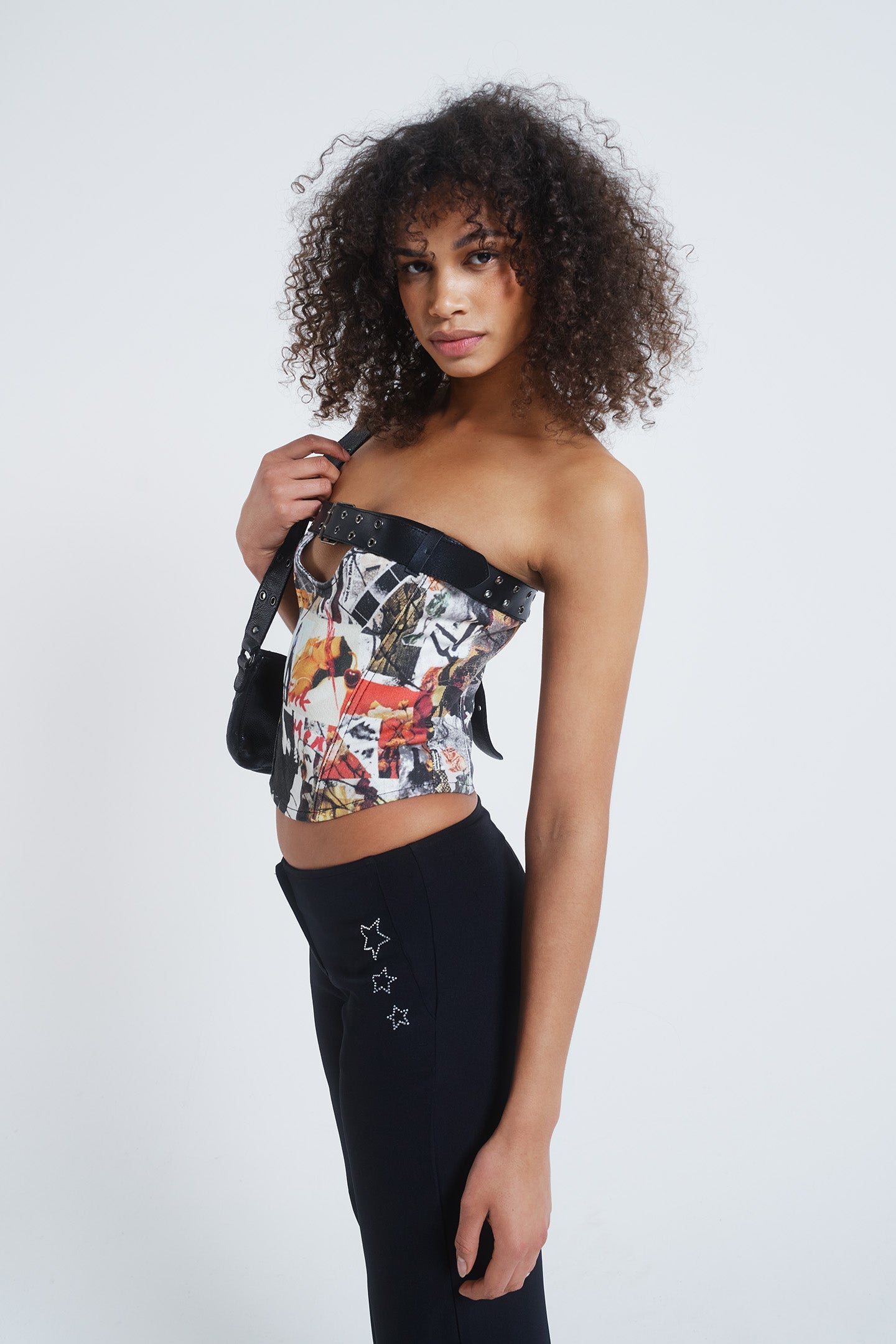 Female model wearing a mixed magazine print corset top with cut out and black belt detail. Paired with black flared trousers.