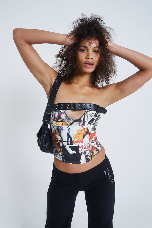 Female model wearing a mixed magazine print corset top with cut out and black belt detail. Paired with black flared trousers.