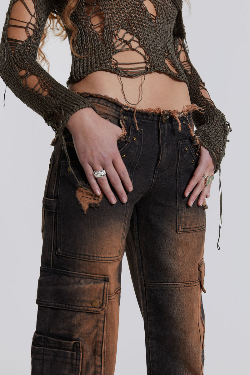 Female model wearing washed black rust cargo denim jeans styled with a khaki green shredded knitted top. 