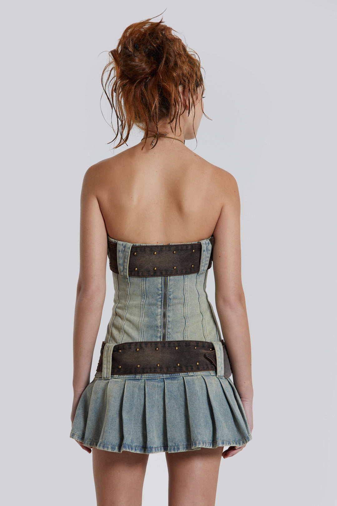 Female model wearing a blue denim pleated mini dress which features a double denim belt detail.  