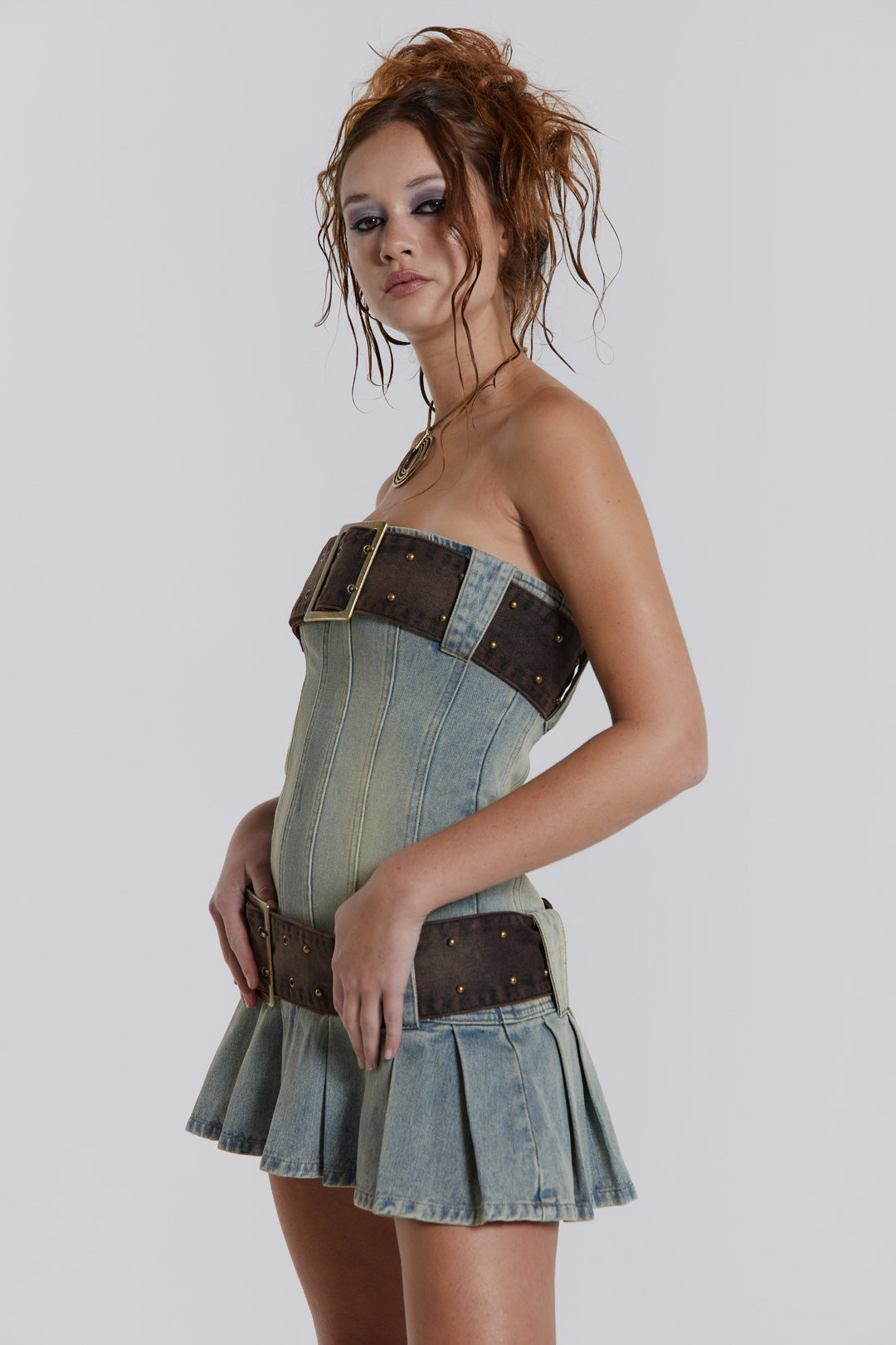 Female model wearing a blue denim pleated mini dress which features a double denim belt detail.  