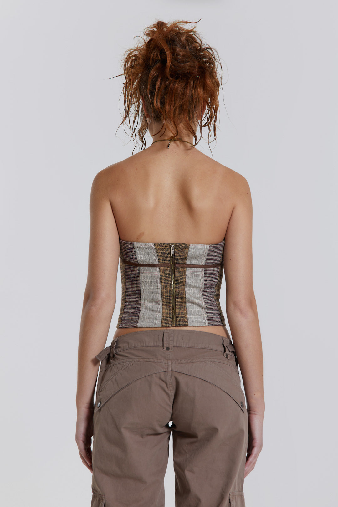 Female model wearing a panelled check corset top with a stitched ribbon detail. Styled with cropped cargo trousers. 