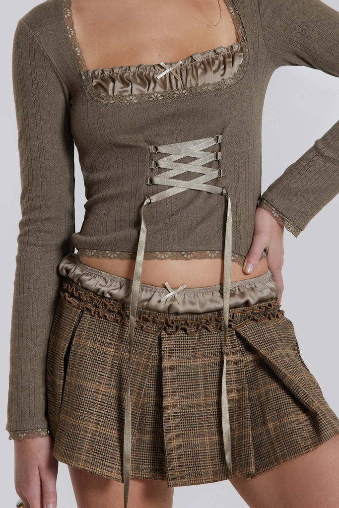 Female model wearing a grey long sleeve bustier top curated from pointelle knit with a satin insert. Styled with a check pleated mini skirt. 