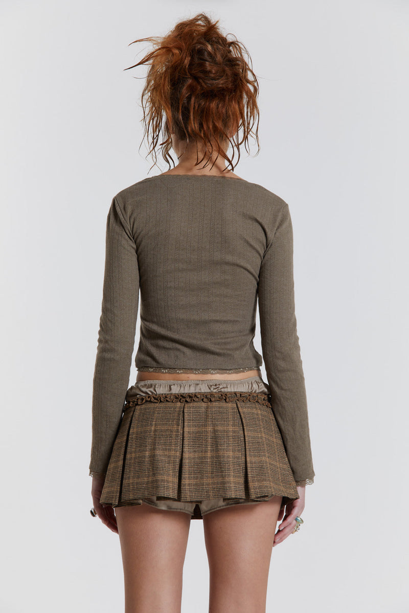 Female model wearing a brown pleated check mini skirt with a satin boxer detail. Paired with a brown knitted long sleeve top. 