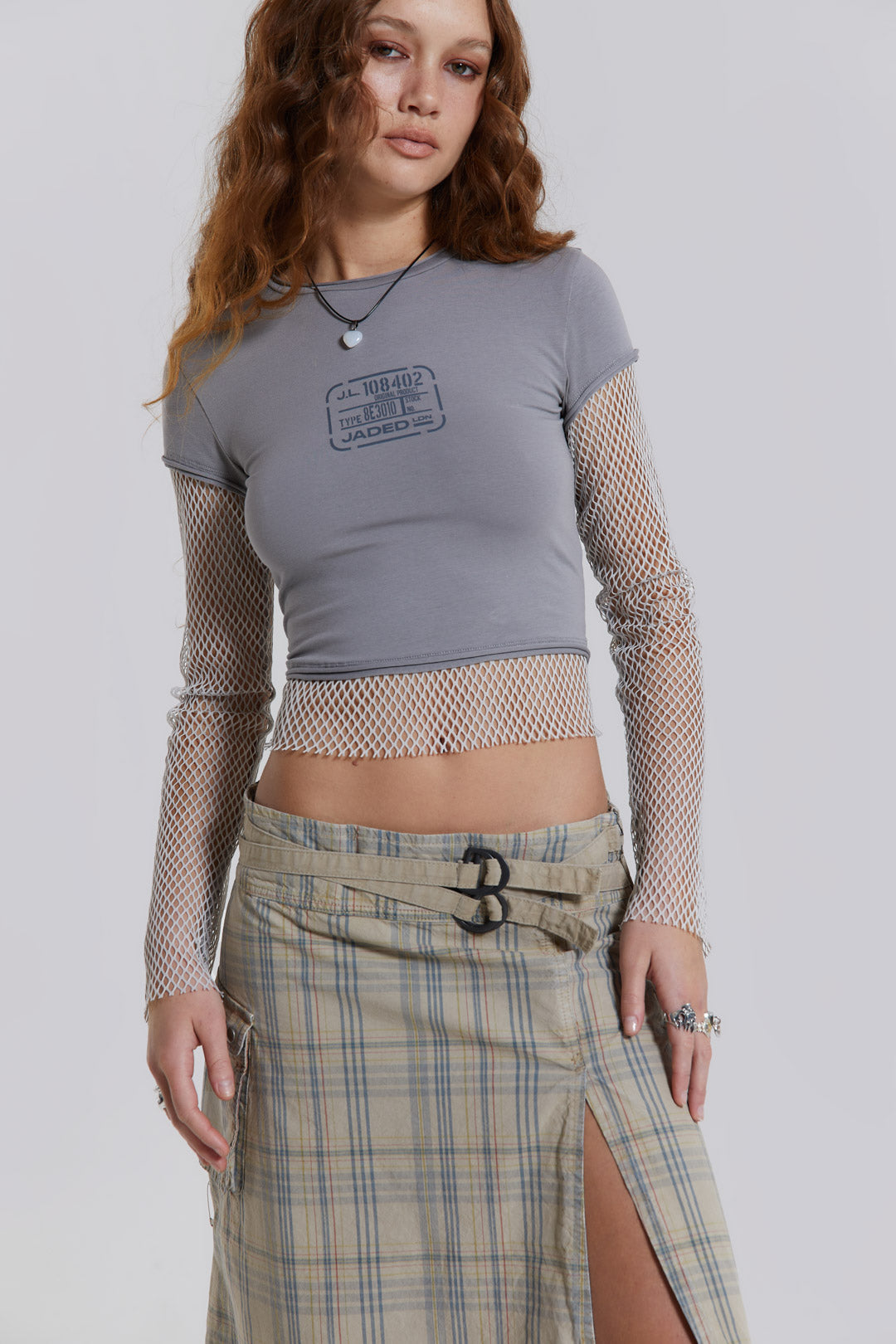 Female model wearing a grey t-shirt with long contrast mesh sleeves, styled with a check midi skirt. 