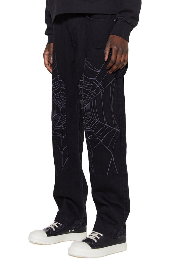 Black spider web print oversized carpenter fit jeans. Styled with black and white trainers and a black hoodie. 