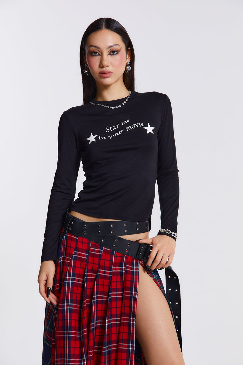 Female model wearing This black long sleeve top features a white movie star screen print graphic across the chest. Styled with a red check maxi skirt.