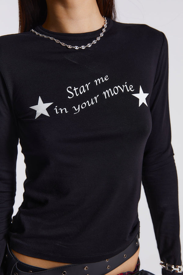 Female model wearing This black long sleeve top features a white movie star screen print graphic across the chest. 