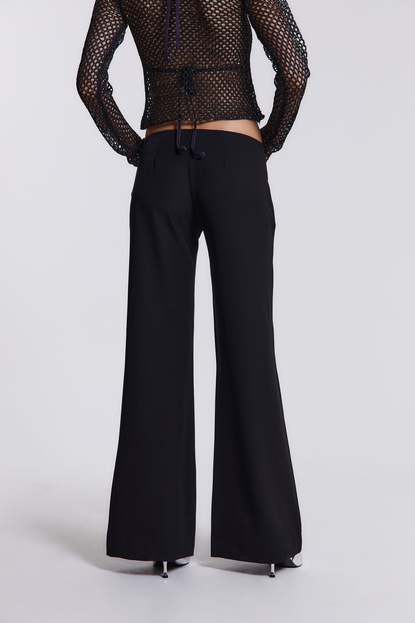 Female model wearing These black low waist trousers are in a wide leg fit and feature a silver diamante star detail.  Paired with a black crochet long sleeve top. 