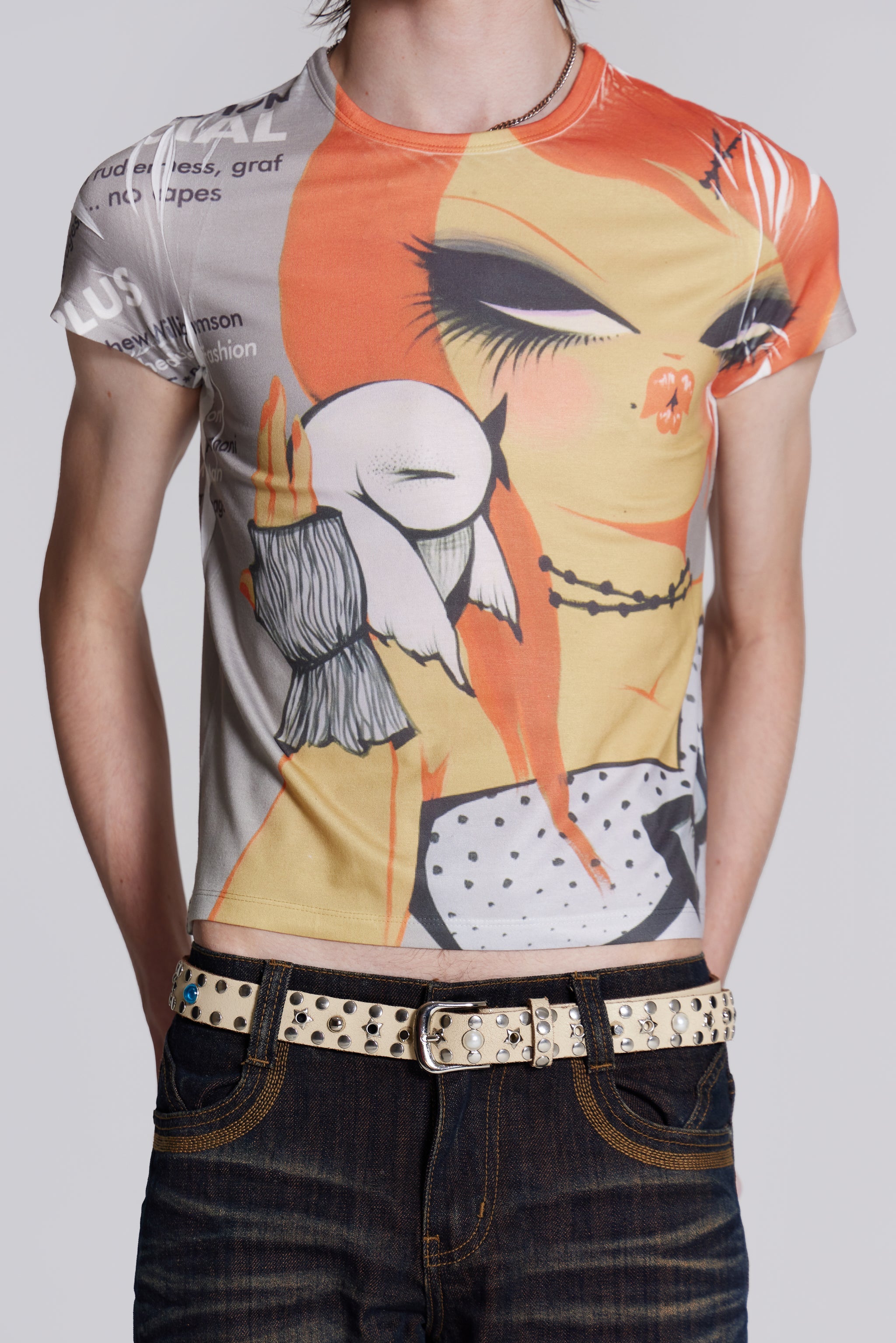 Male wearing graphic print t-shirt styled with denim jeans and studded belt.